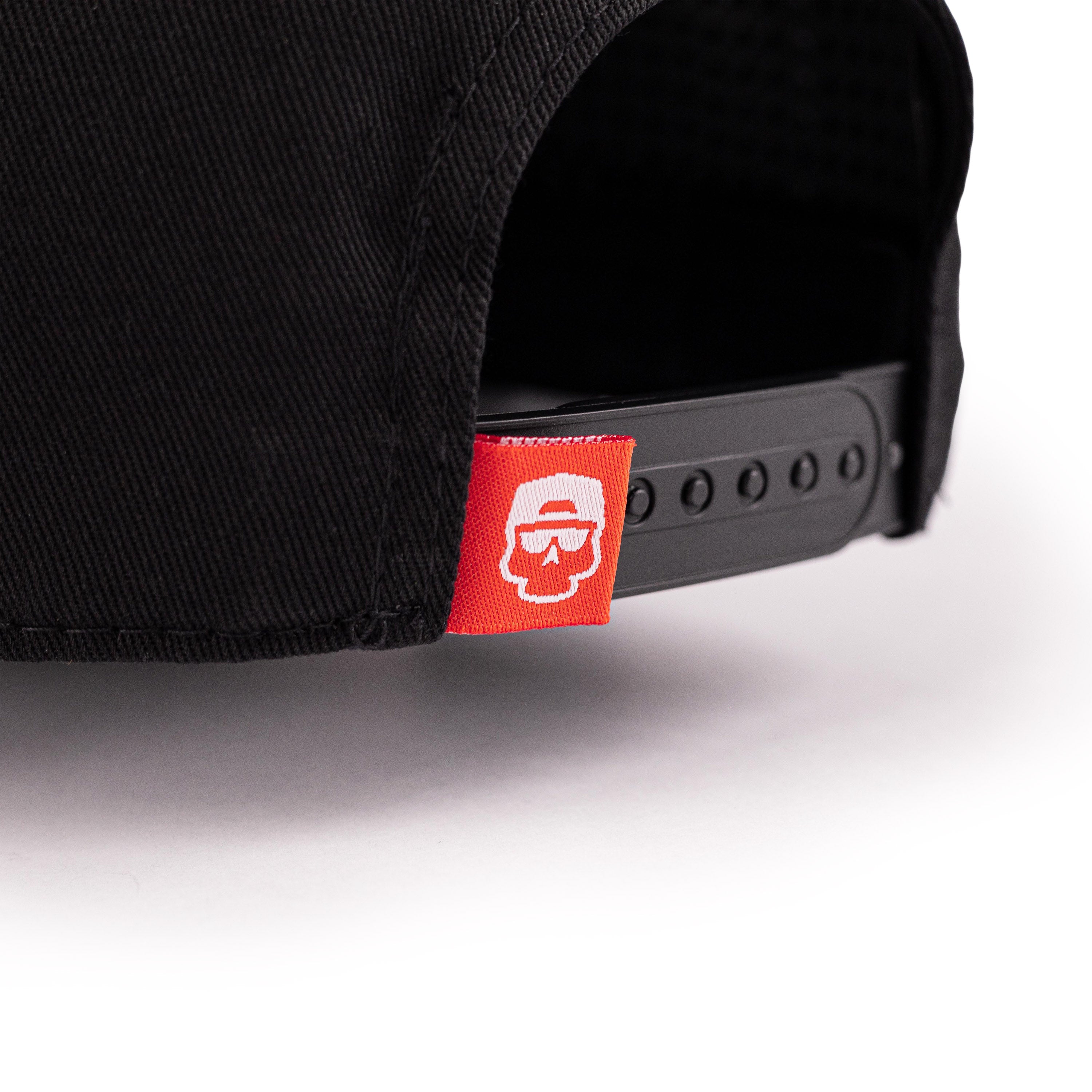 Detail shot of the back of a black baseball cap with red woven label on snapback strap.