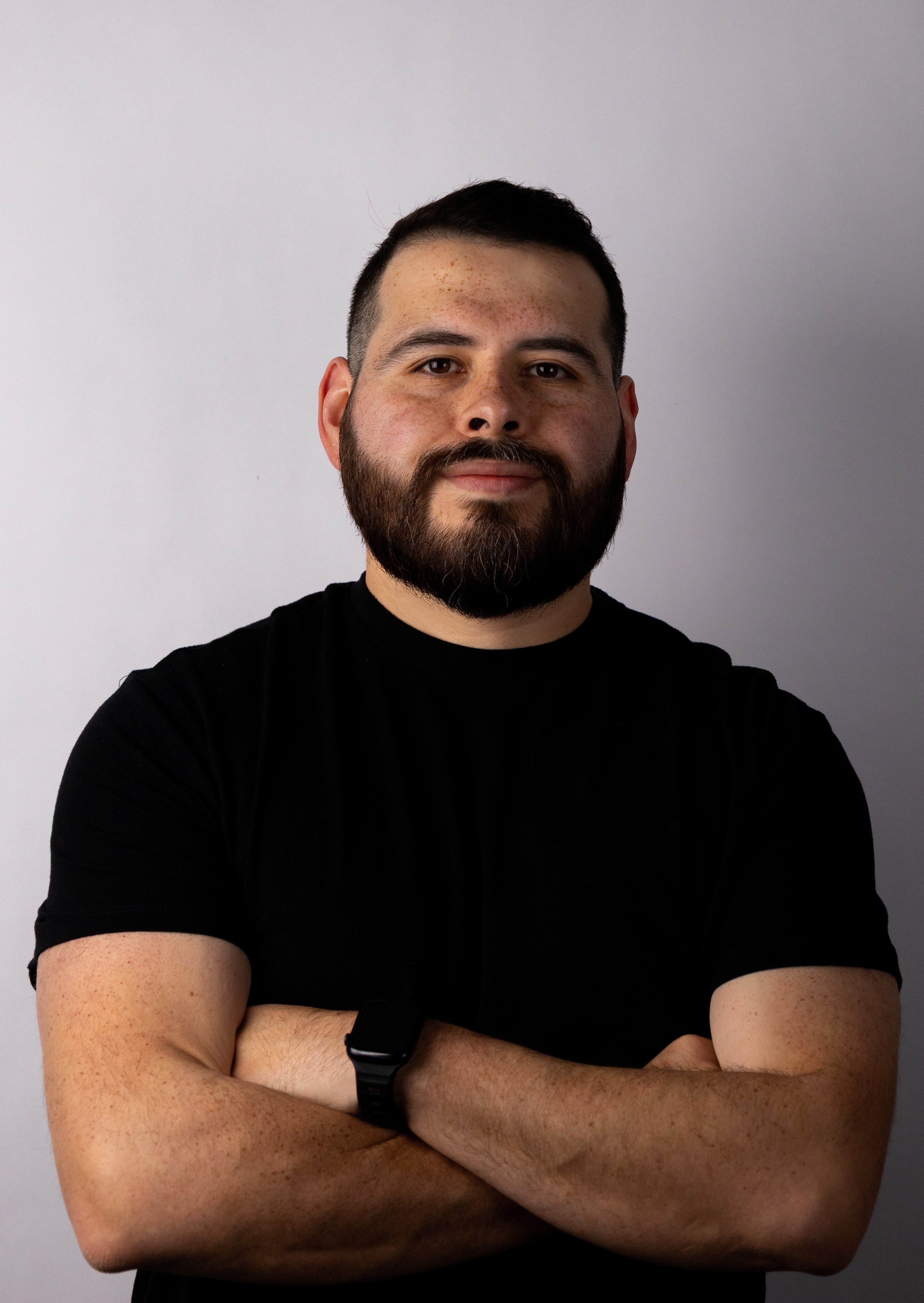 A man standing with his arms crossed wearing a black t-shirt