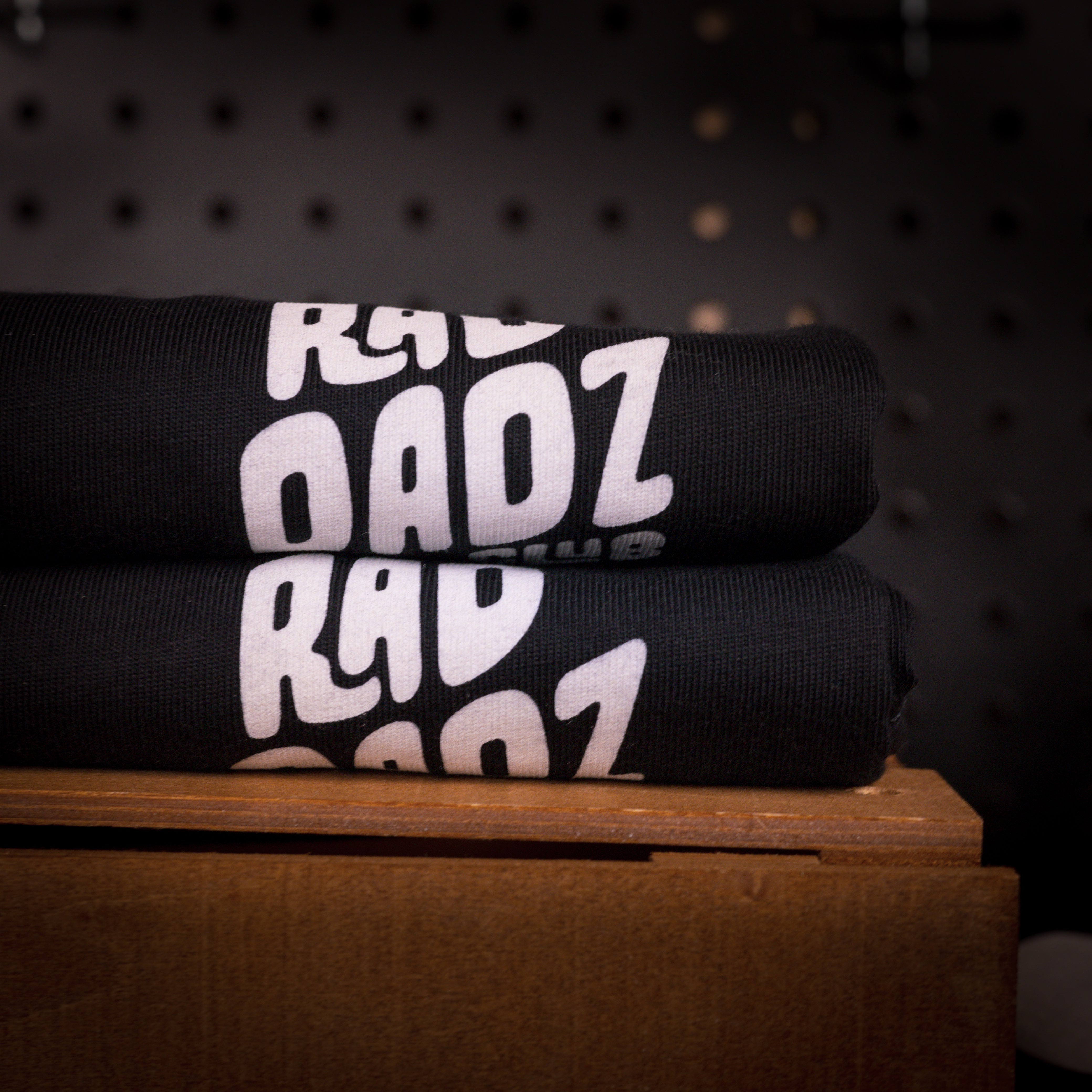 A stack of folded black cotton shirts with a minimal white logo showing.