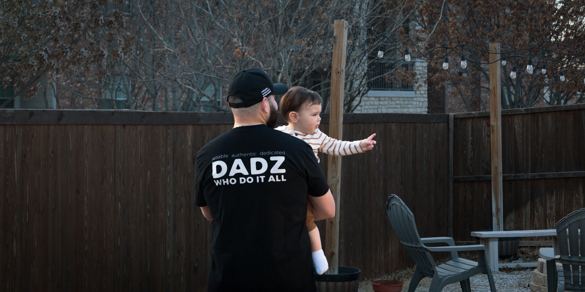 A close-up shot of a black t-shirt with the text 'DADZ WHO DO IT ALL' in white lettering.